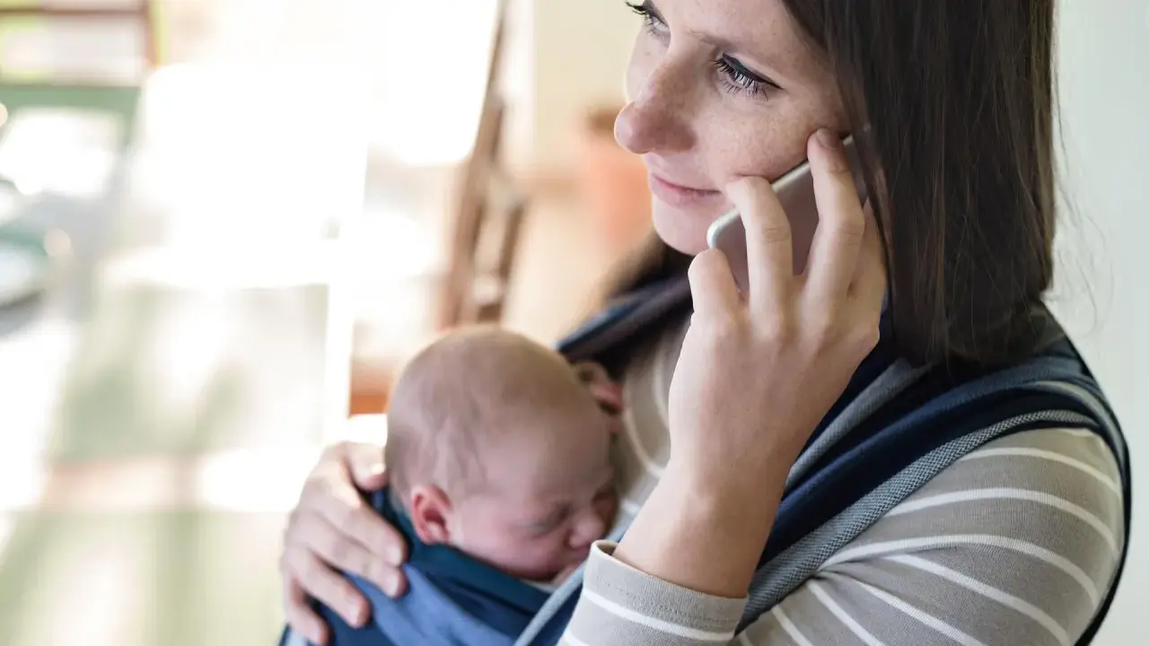 Samotna matka rozmawia przez telefon, trzymając śpiące dziecko w chuście.