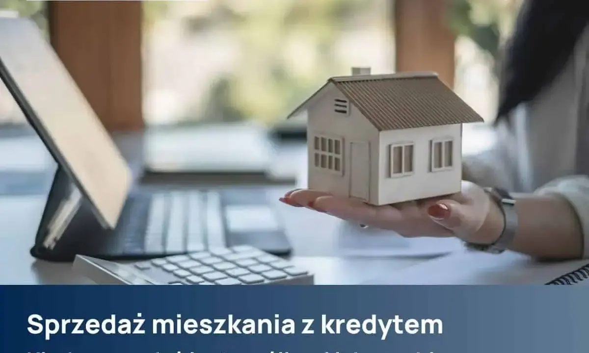 Dłoń trzyma model domu, obok kalkulator i laptop. Temat: sprzedaż mieszkania z kredytem.
