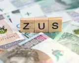 Drewniane klocki z napisem ZUS na tle polskich banknotów. Dowiedz się, ile można dorobić do renty rodzinnej, nie przekraczając limitów ZUS.
