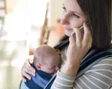 Samotna matka rozmawia przez telefon, trzymając śpiące dziecko w chuście.