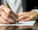 Dłoń pisze piórem na papierze, być może dokumentując służebność mieszkania.