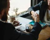 Dwie osoby w garniturach ściskają sobie dłonie przy stoliku z kawą.