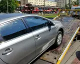 Srebrny samochód jest ładowany na lawetę. Pracownik w żółtej koszulce zabezpiecza pojazd, co może oznaczać konfiskatę samochodu.