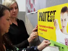 Dwie kobiety wieszają plakat "PROTEST WŁOSKI" na tablicy. Hasło głosi: "To jest protest w obronie naszej godności!".