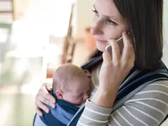 Samotna matka rozmawia przez telefon, trzymając śpiące dziecko w chuście.