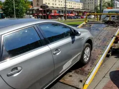 Srebrny samochód jest ładowany na lawetę. Pracownik w żółtej koszulce zabezpiecza pojazd, co może oznaczać konfiskatę samochodu.
