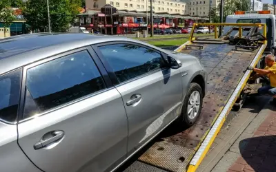 Srebrny samochód jest ładowany na lawetę. Pracownik w żółtej koszulce zabezpiecza pojazd, co może oznaczać konfiskatę samochodu.