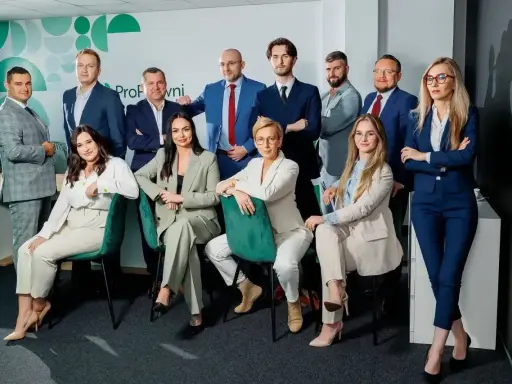 Grupa prawników w eleganckich garniturach pozuje do zdjęcia w nowoczesnym biurze.