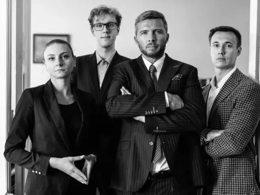 Cztery osoby w garniturach, w tym dwie kobiety i dwóch mężczyzn, stoją w rzędzie.