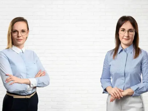 Dwie kobiety w koszulach na tle białej ceglanej ściany.