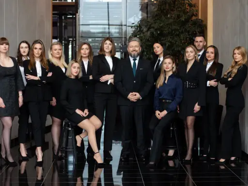 Grupa prawników i radców prawnych w eleganckich strojach stoi w nowoczesnym wnętrzu.