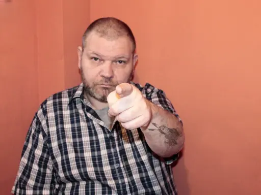 Mężczyzna w kratę wskazuje palcem, na ramieniu ma tatuaż Indianina. To jest 234 kk.