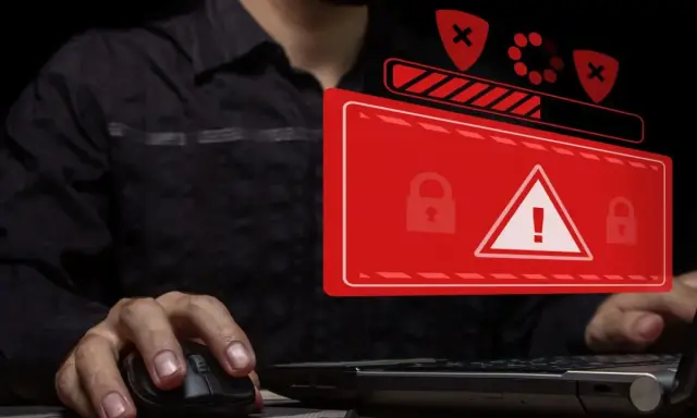 Osoba przy komputerze, na ekranie ostrzeżenie o zagrożeniu i blokadzie. To obrazuje problem cyberprzestępczości.