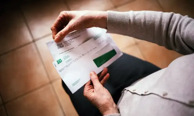 Dłonie trzymają kopertę ZUS. W środku decyzja o waloryzacji emerytury, być może zapowiedź trzynastej emerytury.