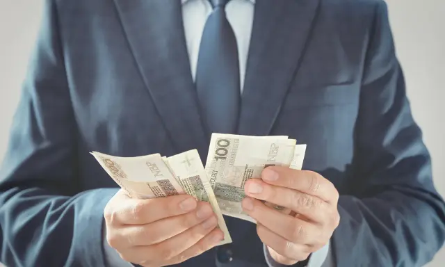 Mężczyzna w garniturze liczy banknoty 100 zł. To jego zabezpieczenie finansowe na przyszłość.