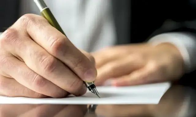 Dłoń pisze piórem na papierze, być może dokumentując służebność mieszkania.