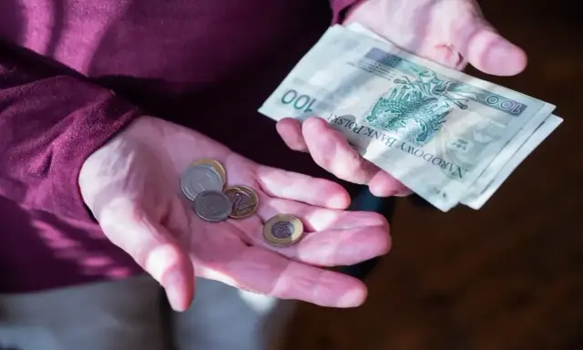 Dłonie trzymające polskie banknoty i monety. Zastanawiasz się, ile wynosi dodatek do emerytury za warunki szkodliwe?
