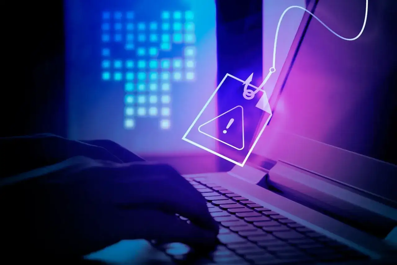 Ręce na klawiaturze, symbol ostrzeżenia na haczyku. Dowiedz się, gdzie zgłosić oszustwo internetowe i chroń się przed cyberzagrożeniami.