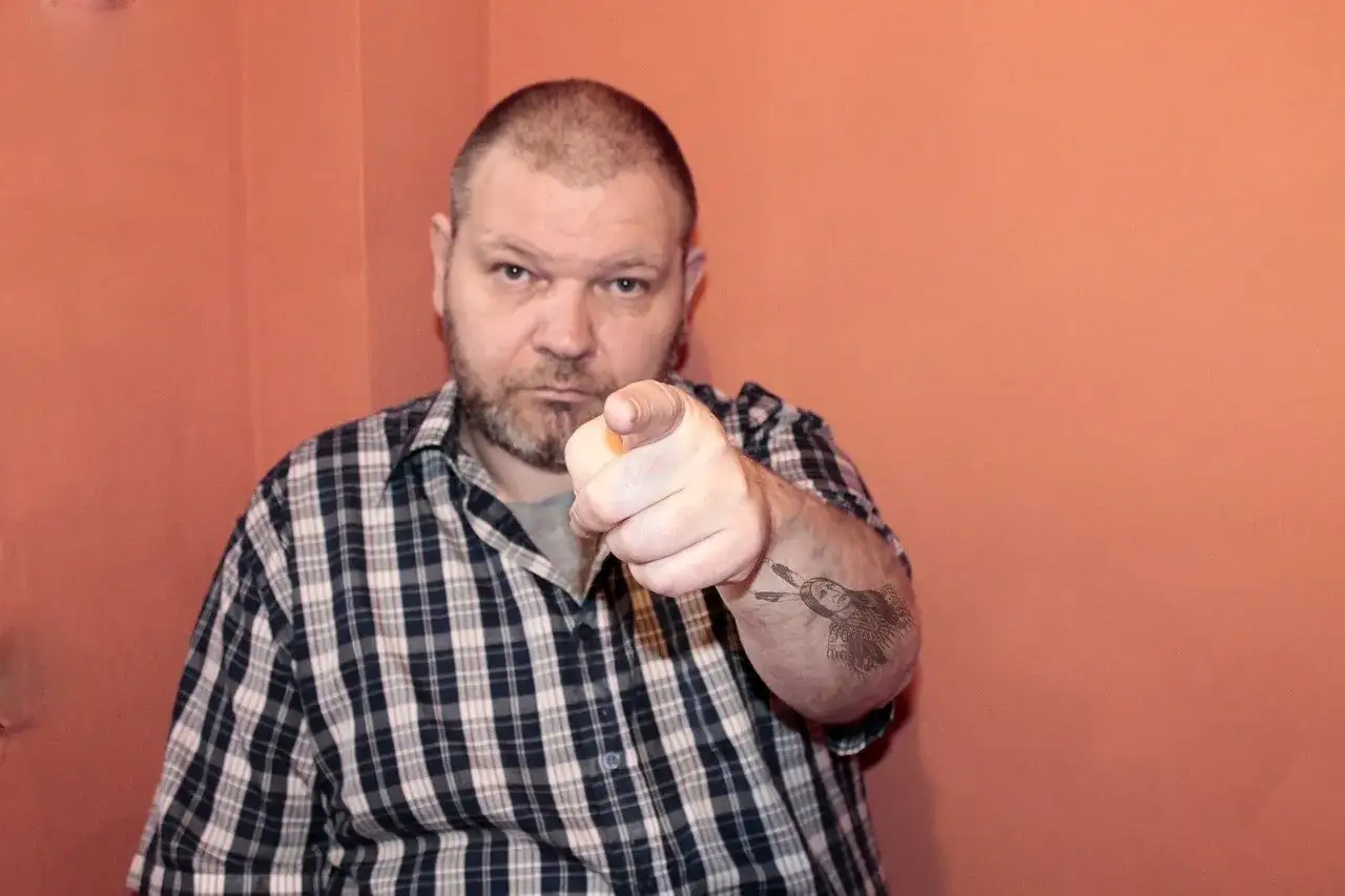 Mężczyzna w kratę wskazuje palcem, jakby mówił 