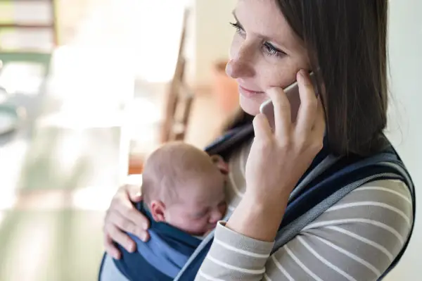 Samotna matka rozmawia przez telefon, trzymając śpiące dziecko w chuście.