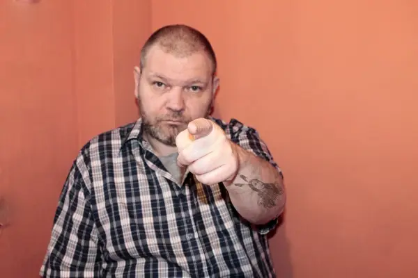 Mężczyzna w kratę wskazuje palcem, na ramieniu ma tatuaż Indianina. To jest 234 kk.