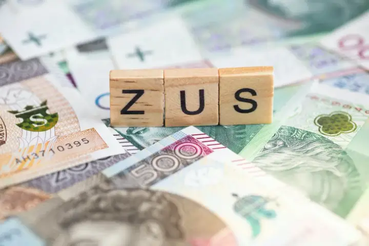 Drewniane klocki z napisem ZUS na tle polskich banknotów. Dowiedz się, ile można dorobić do renty rodzinnej, nie przekraczając limitów ZUS.