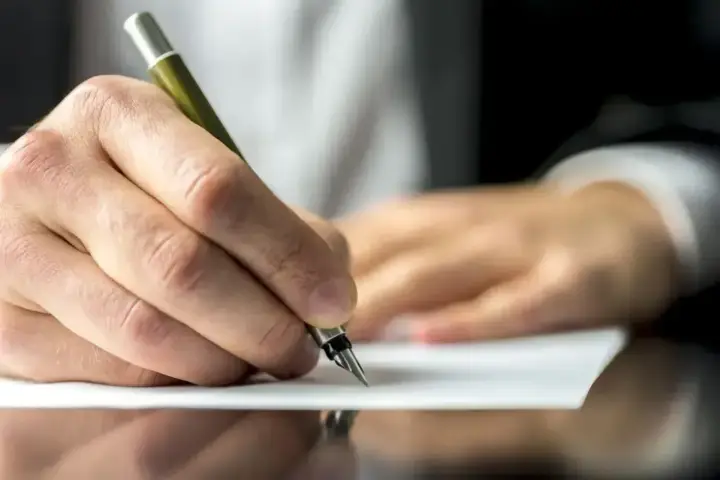Dłoń pisze piórem na papierze, być może dokumentując służebność mieszkania.